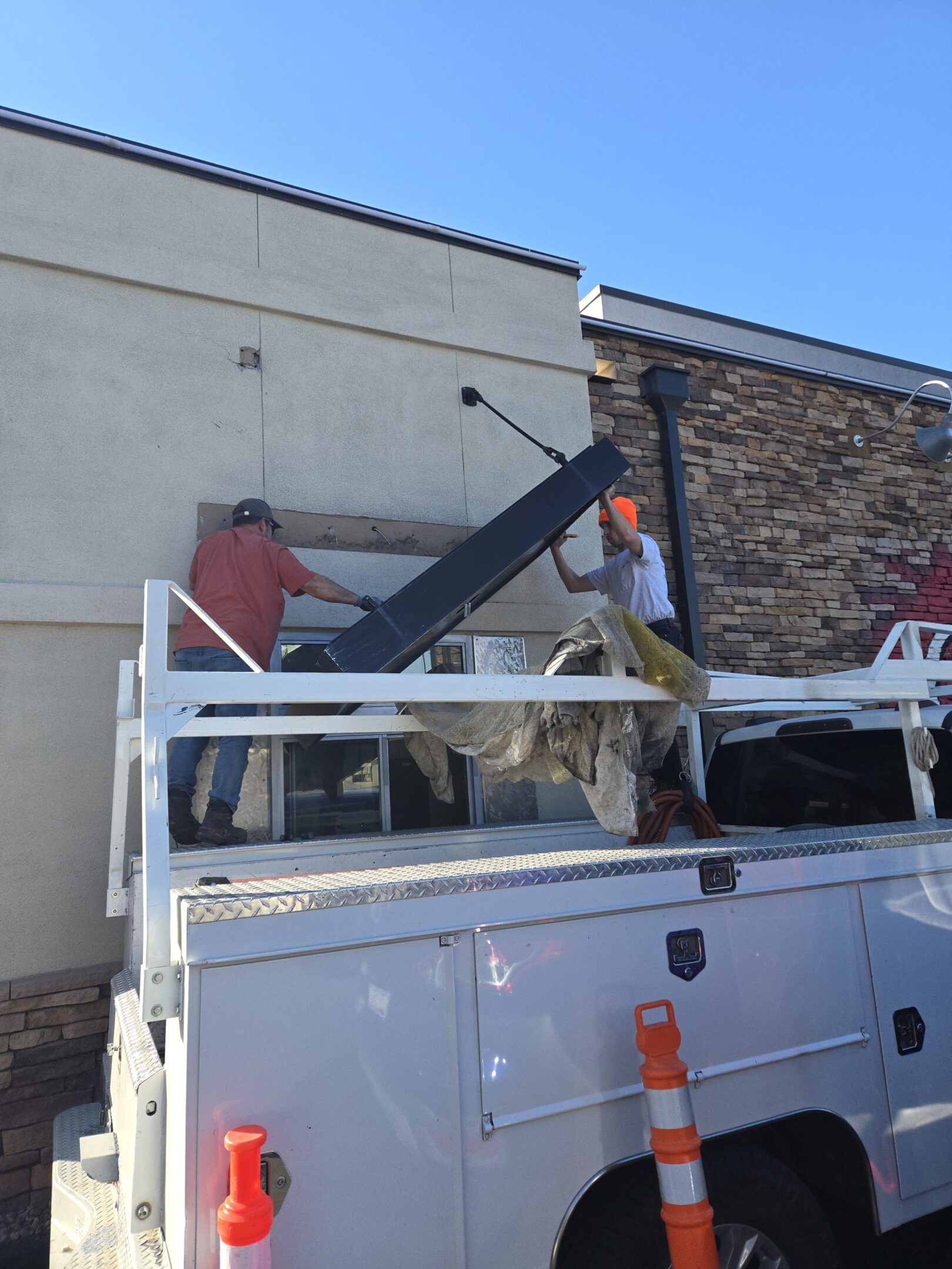 Two workers installing or repairing a large sign on a building roof.