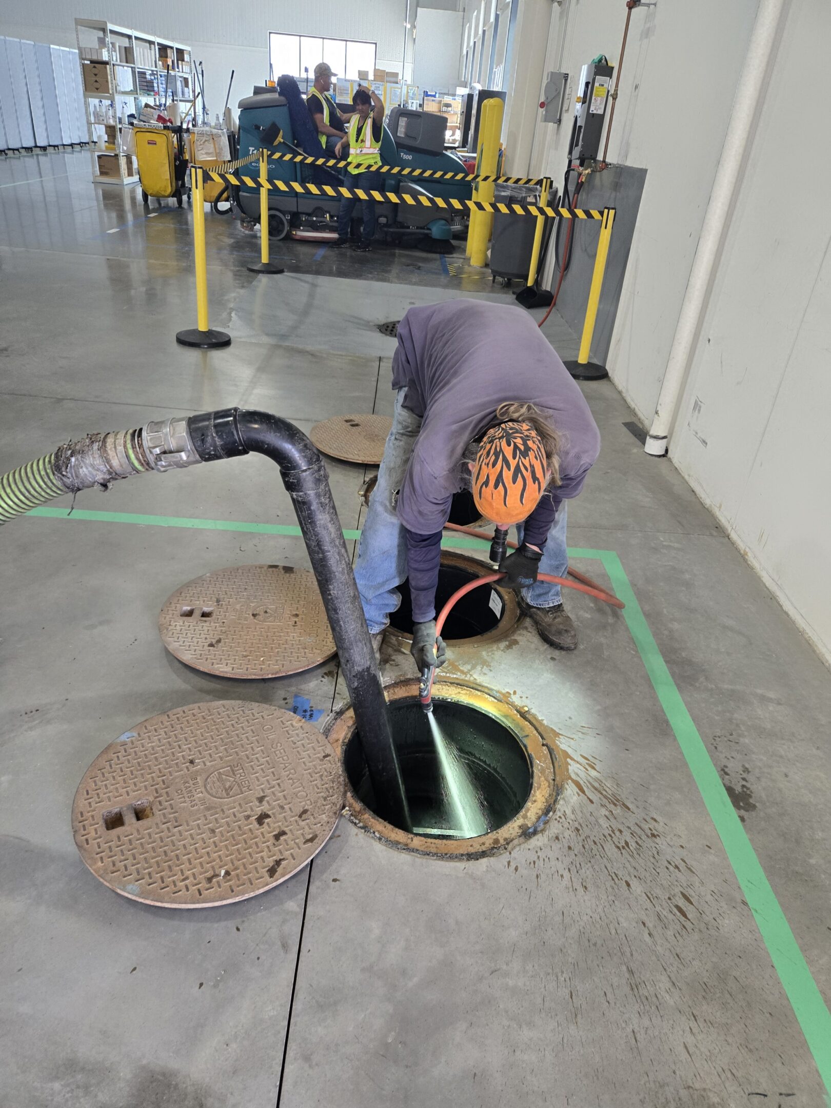 Worker inspecting a manhole with safety gear in an industrial setting.