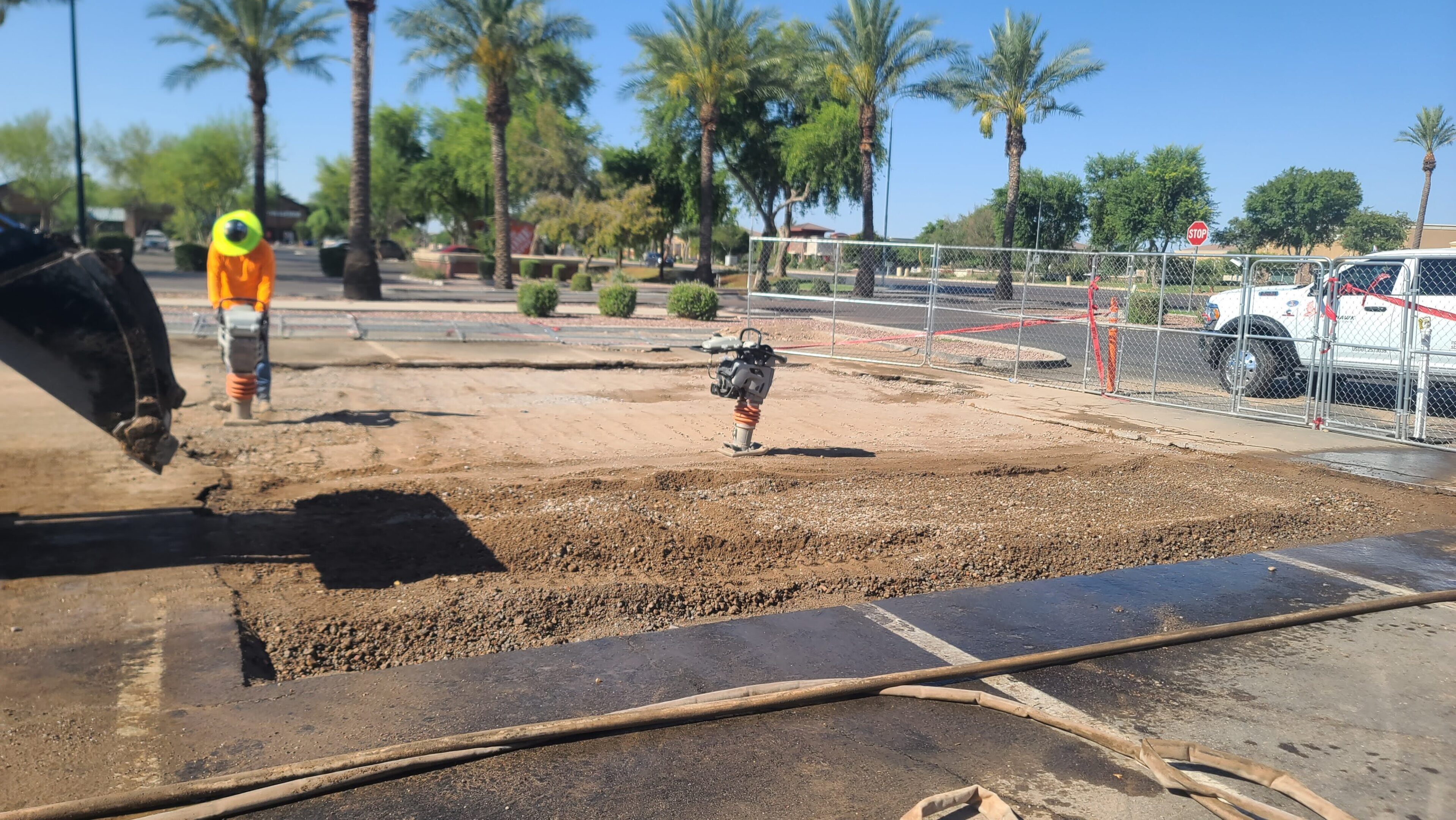 Construction site with soil and palm trees under a clear blue sky.