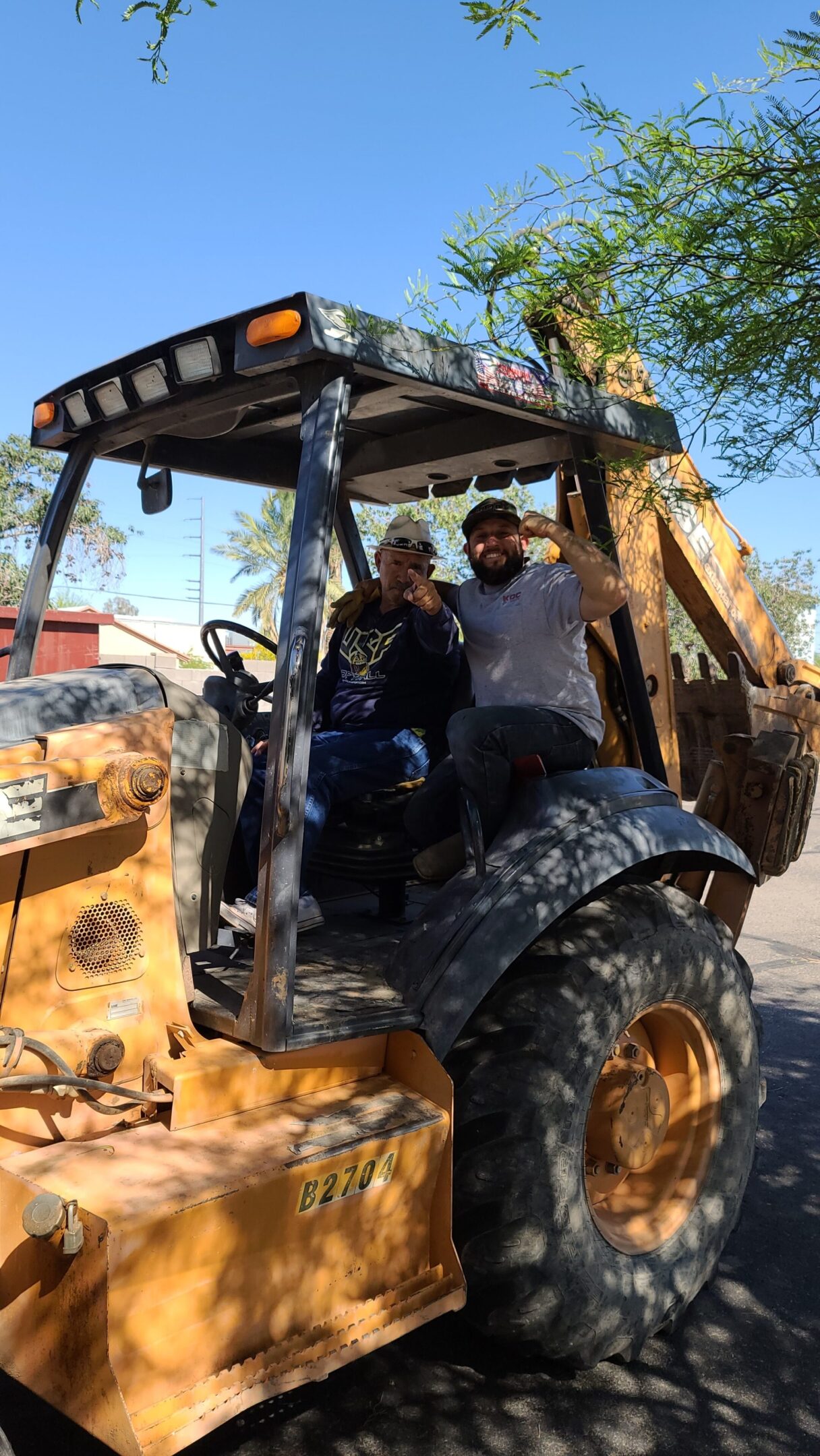 Two men posing inside an old construction vehicle on a sunny day.